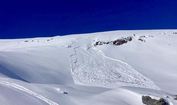 a track in the foreground and avalanche in the distance below a wind-loaded ridge. 