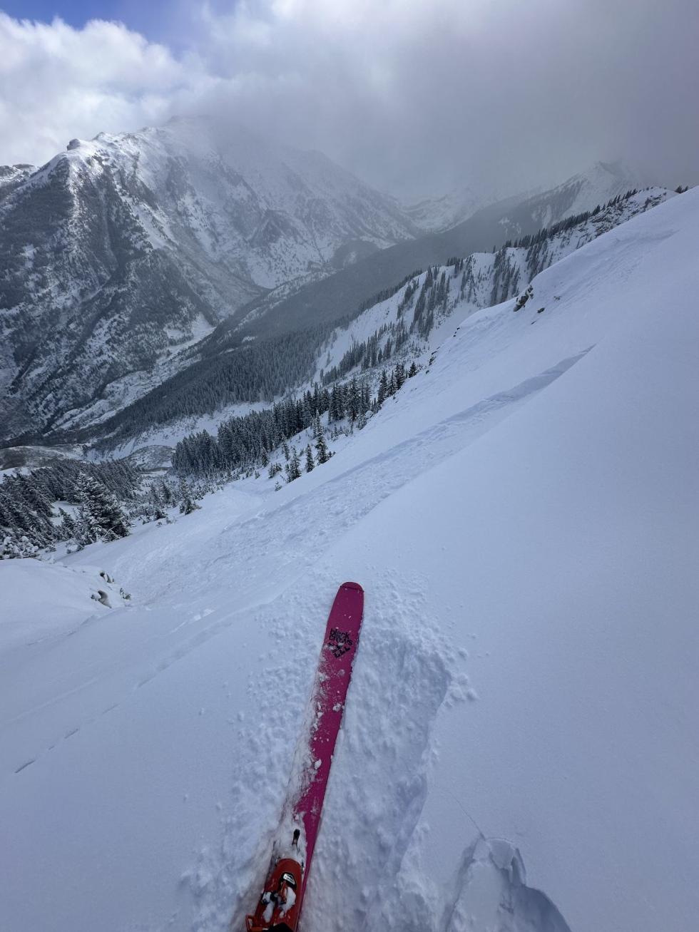 Looking down is a red ski in wind drifted snow and an avalanche on the steep slope below. 